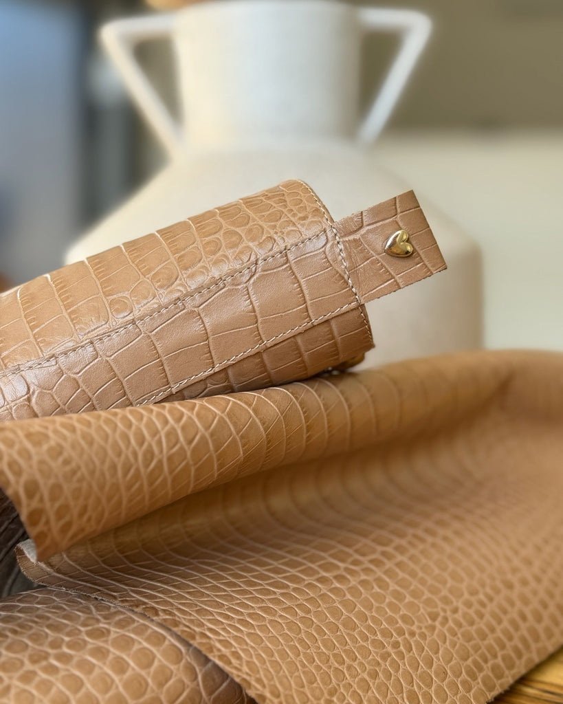 Close-up of beige croco with a heart-shaped metal clip on a blurred background